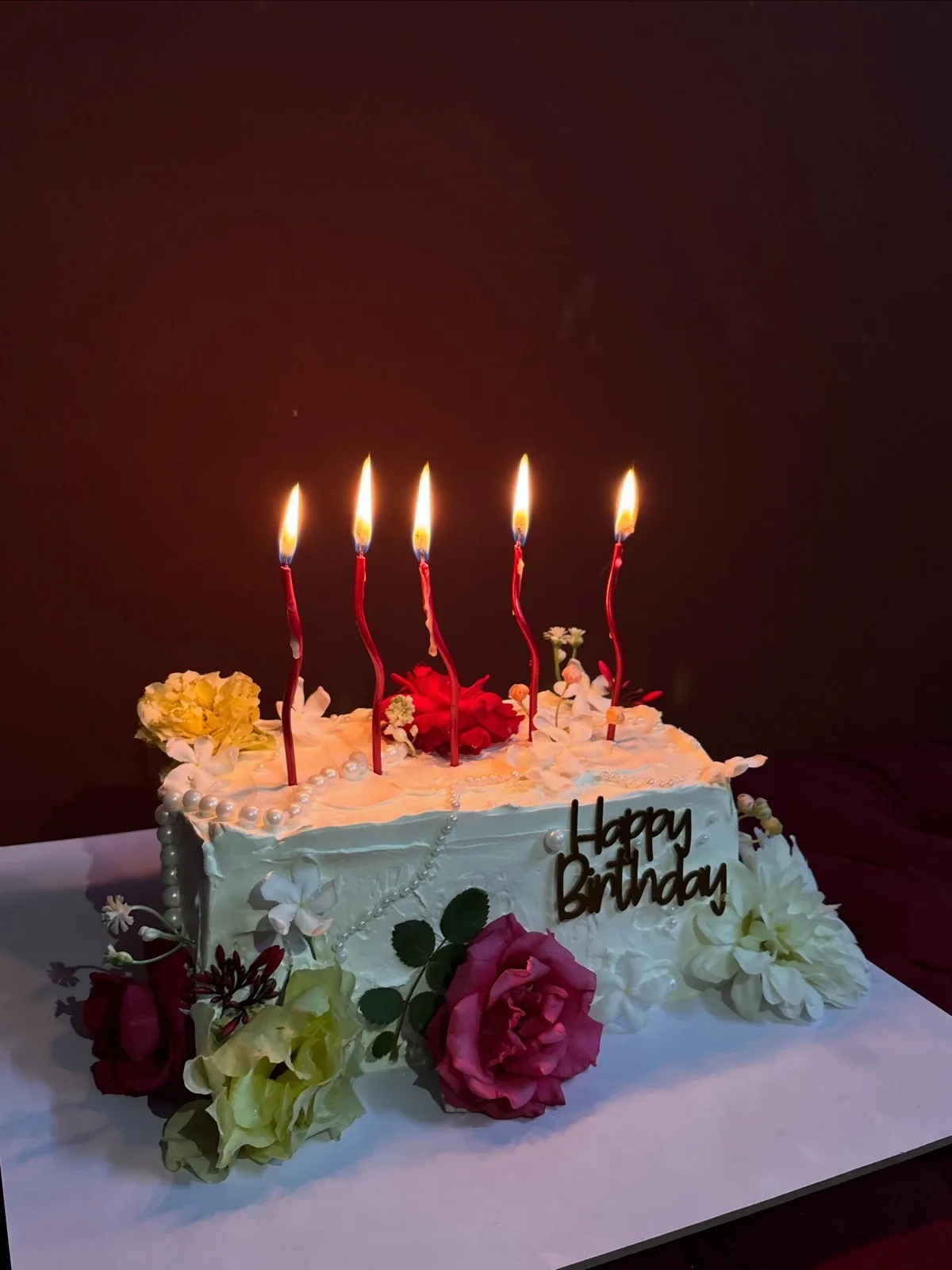 Buttercream birthday cake with lit candles and fresh flowers