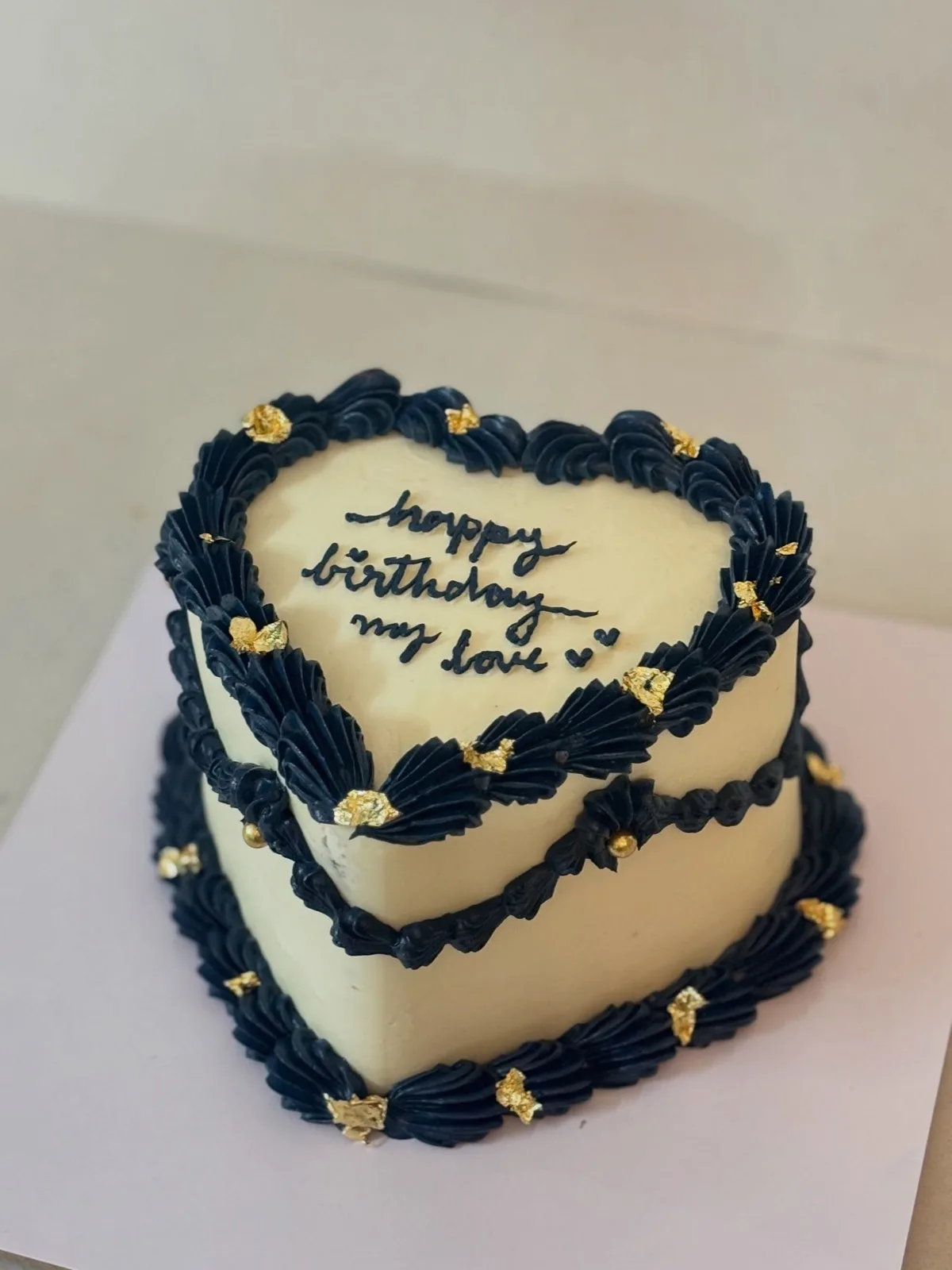 Two-tier heart cake in navy and cream with gold leaf
