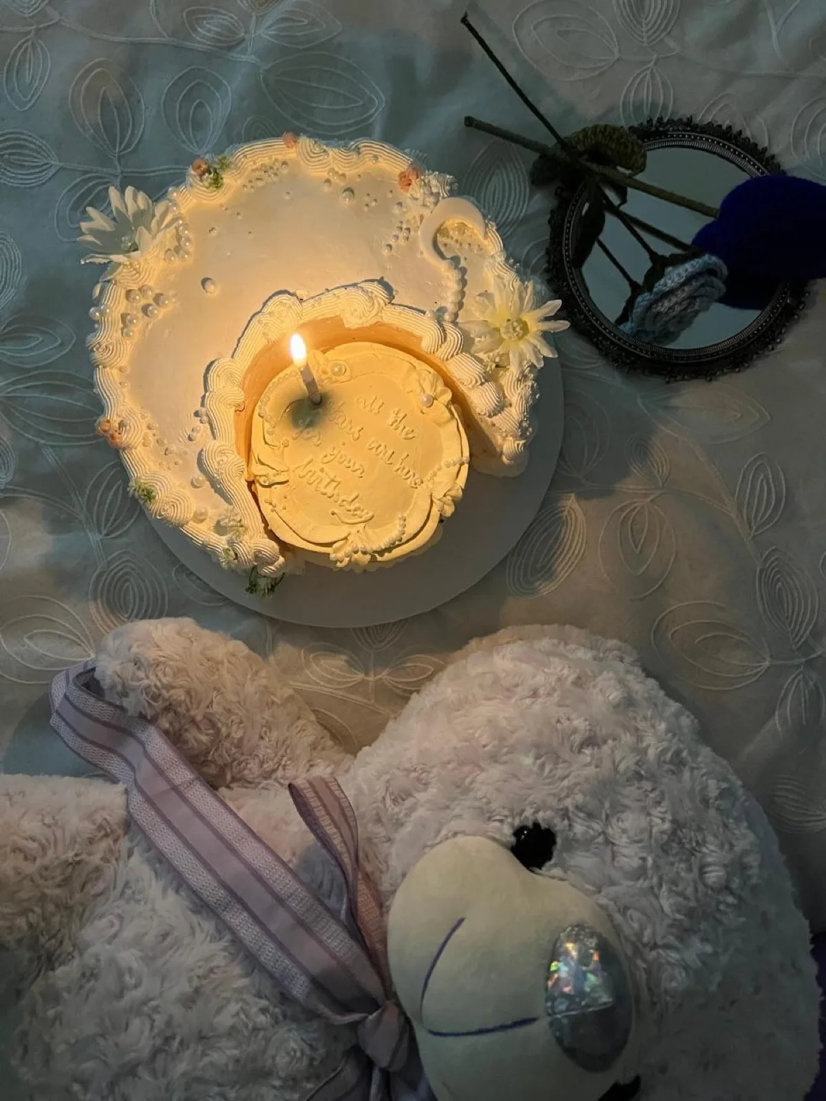 White floral cake with a single candle, styled with a teddy bear