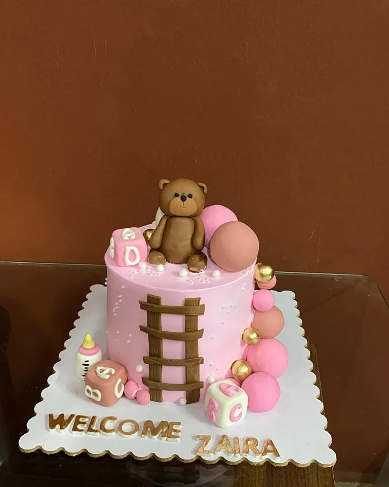 Pink welcome baby cake with a fondant teddy bear, ladder and name blocks