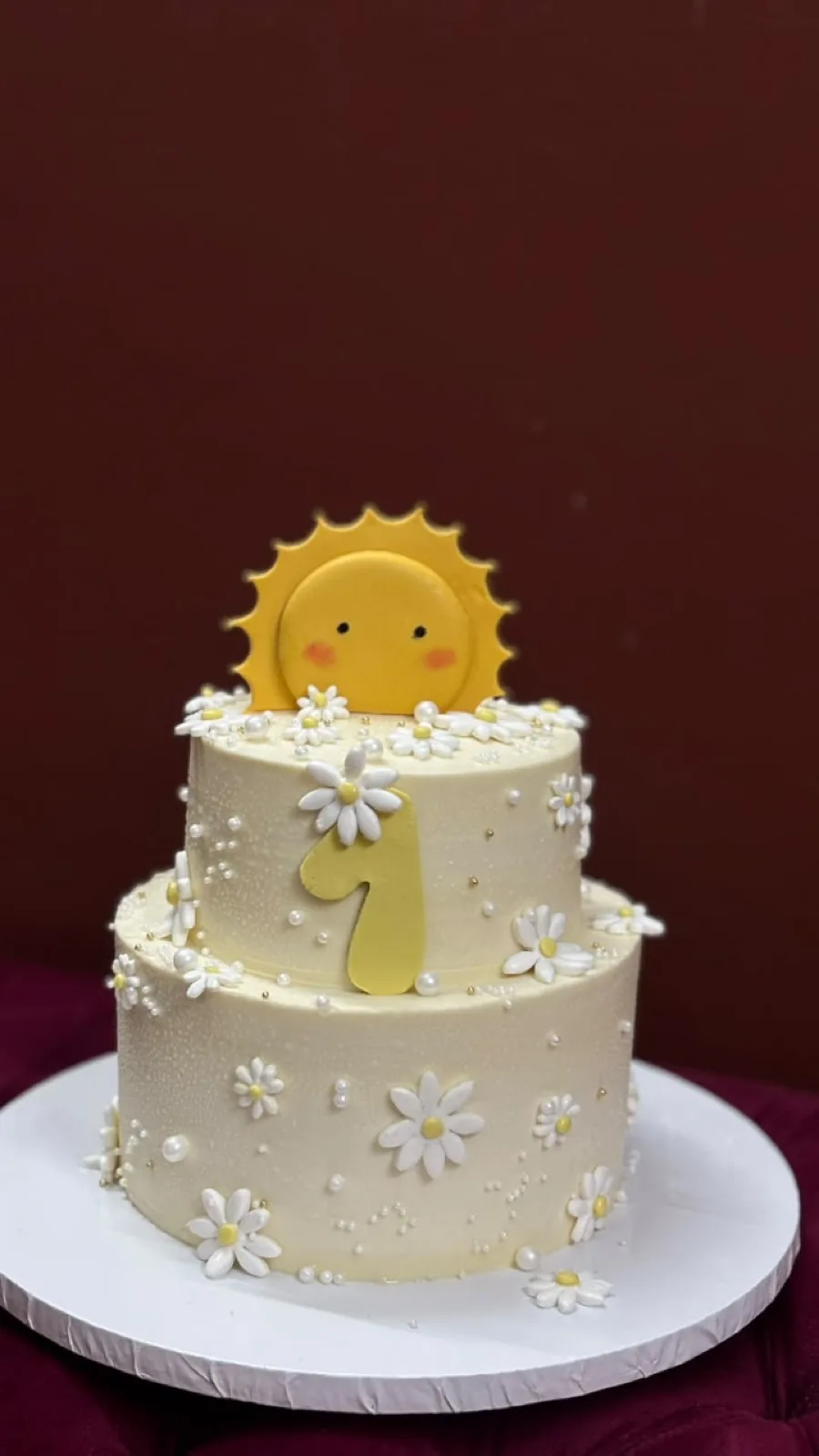 Two-tier first birthday cake with daisies, pearls and a fondant sun topper
