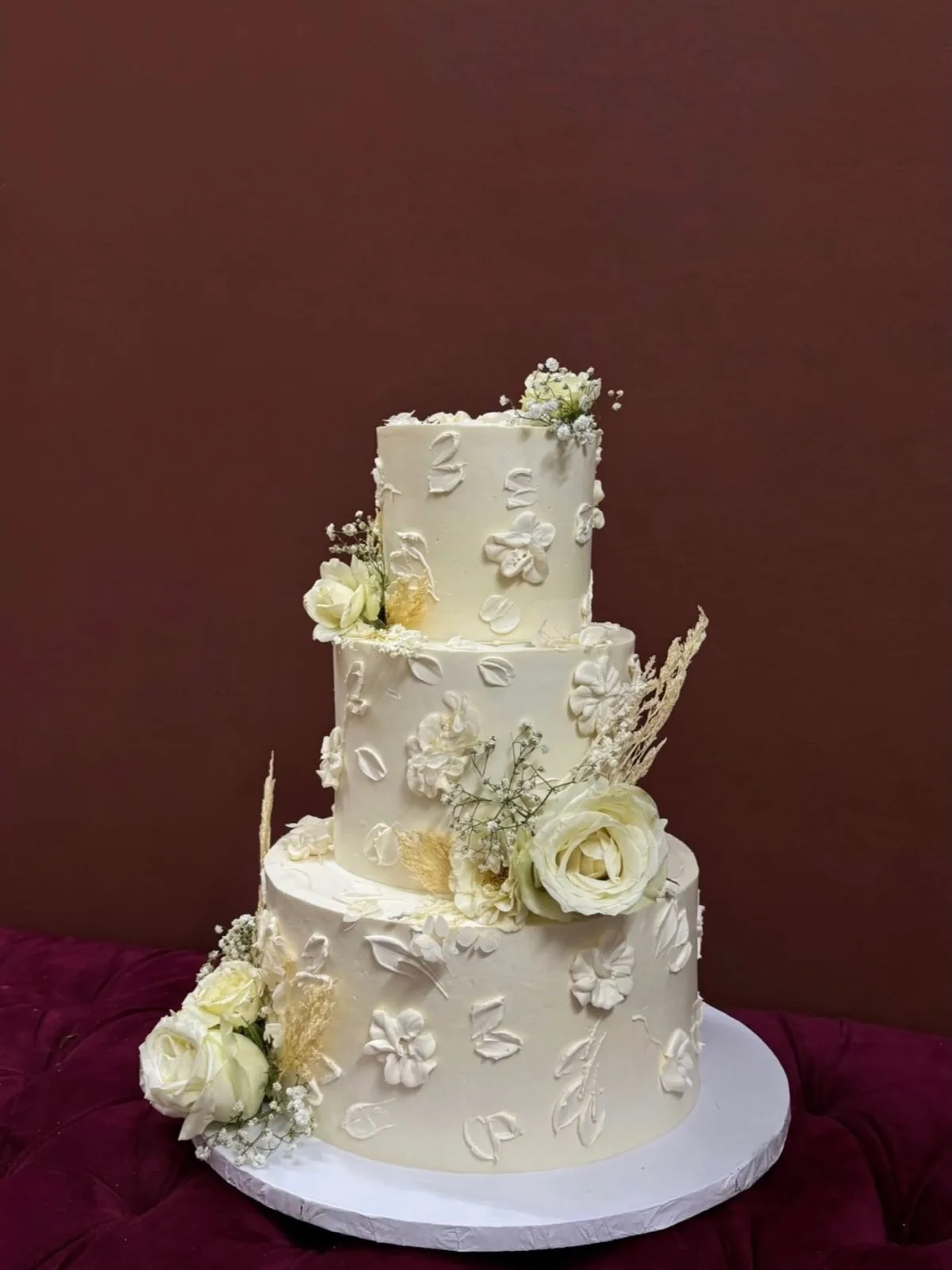 Three-tier ivory wedding cake with piped blossoms and fresh roses