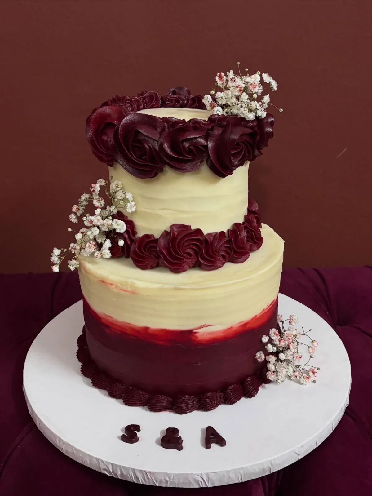 Two-tier maroon and cream cake with piped roses