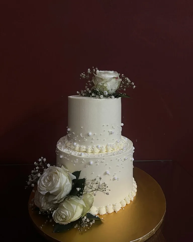 Two-tier white wedding cake with piped pearls, white roses and baby's breath