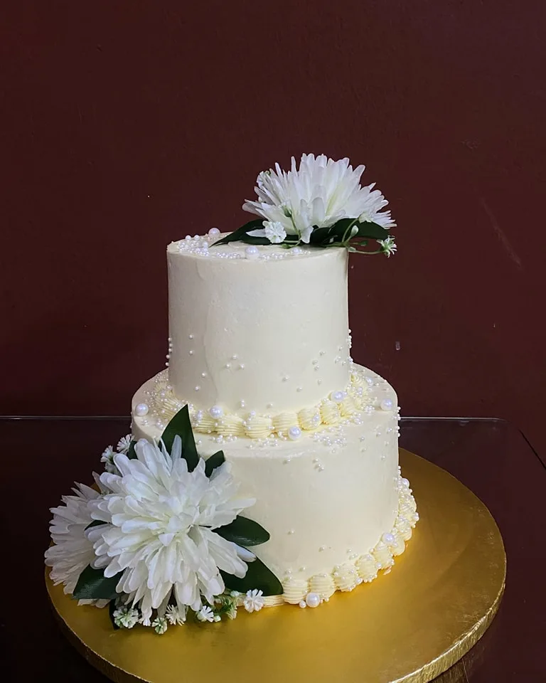 Two-tier ivory wedding cake with white chrysanthemums on a gold board